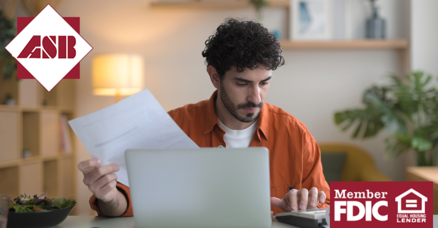 Young man holding files and using calculator in front of his laptop