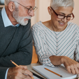 Older man and woman looking down at a notebook with pencils in hand