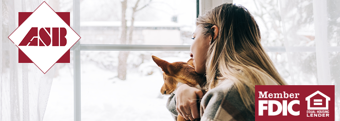 Woman snuggling her dog and looking outside at snowy yard