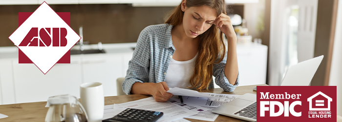 A young adult woman looking stressed at papers and laptop